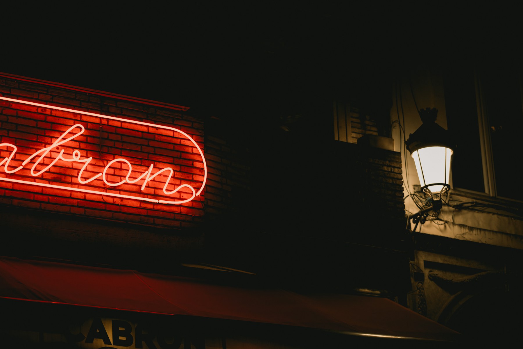 A red neon sign illuminates a dark city street