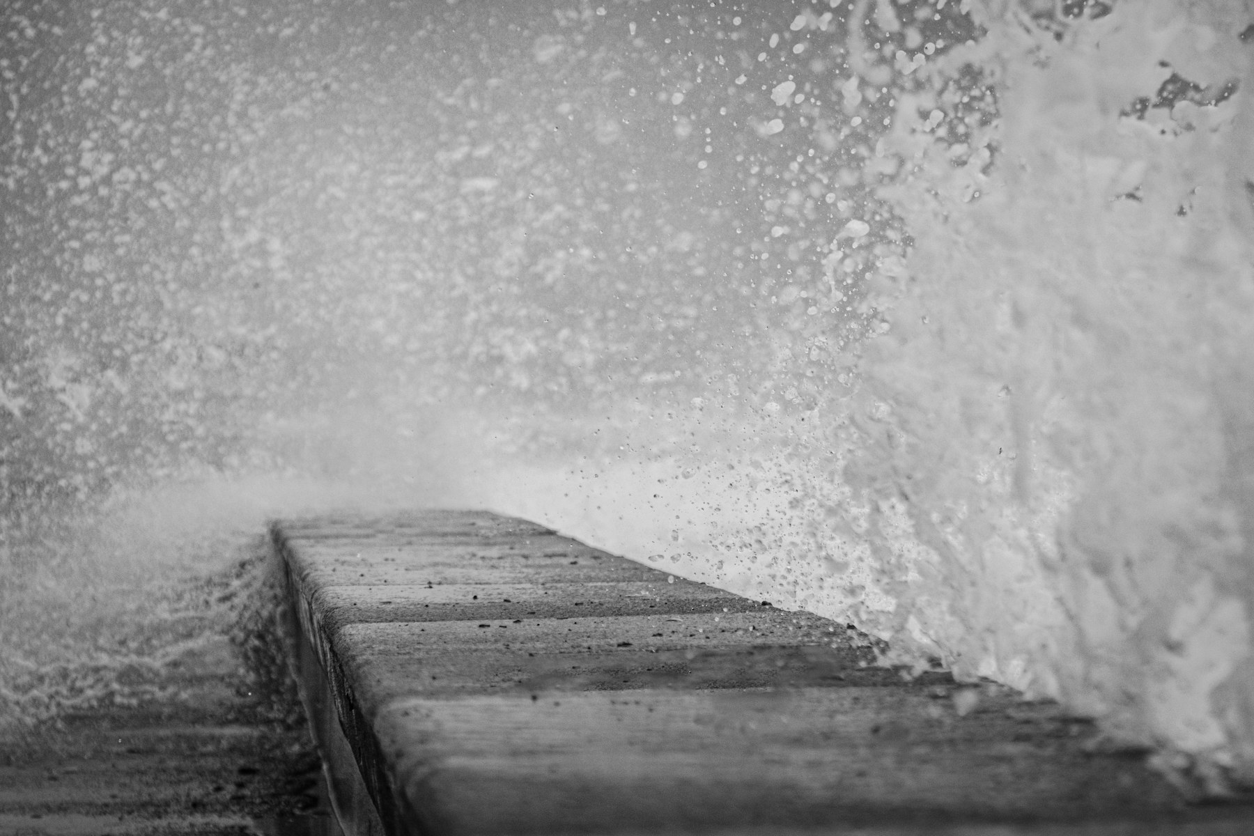 A wave crashes across a pier in black and white